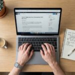 A man typing on a laptop with keyword research notes on a clean desk.
